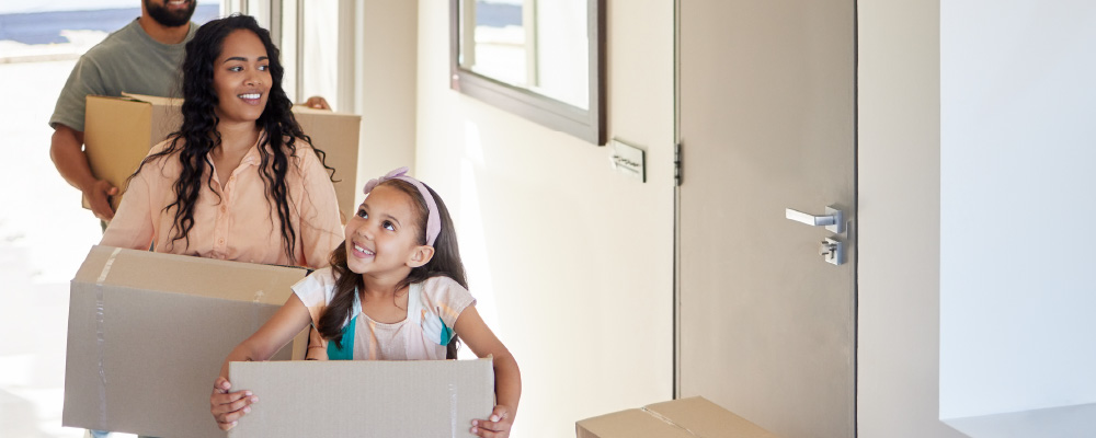 A mom and young daughter carrying boxes into their new home